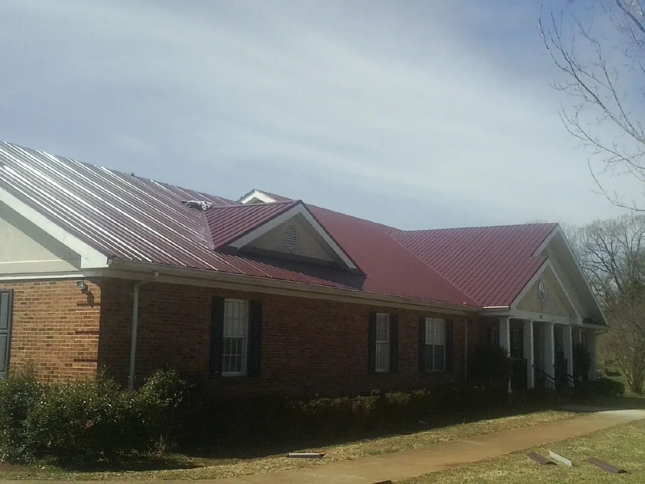Red metal roof with gabled entries on a long brick building, from a Hail Damage Roof Repair job in Paris